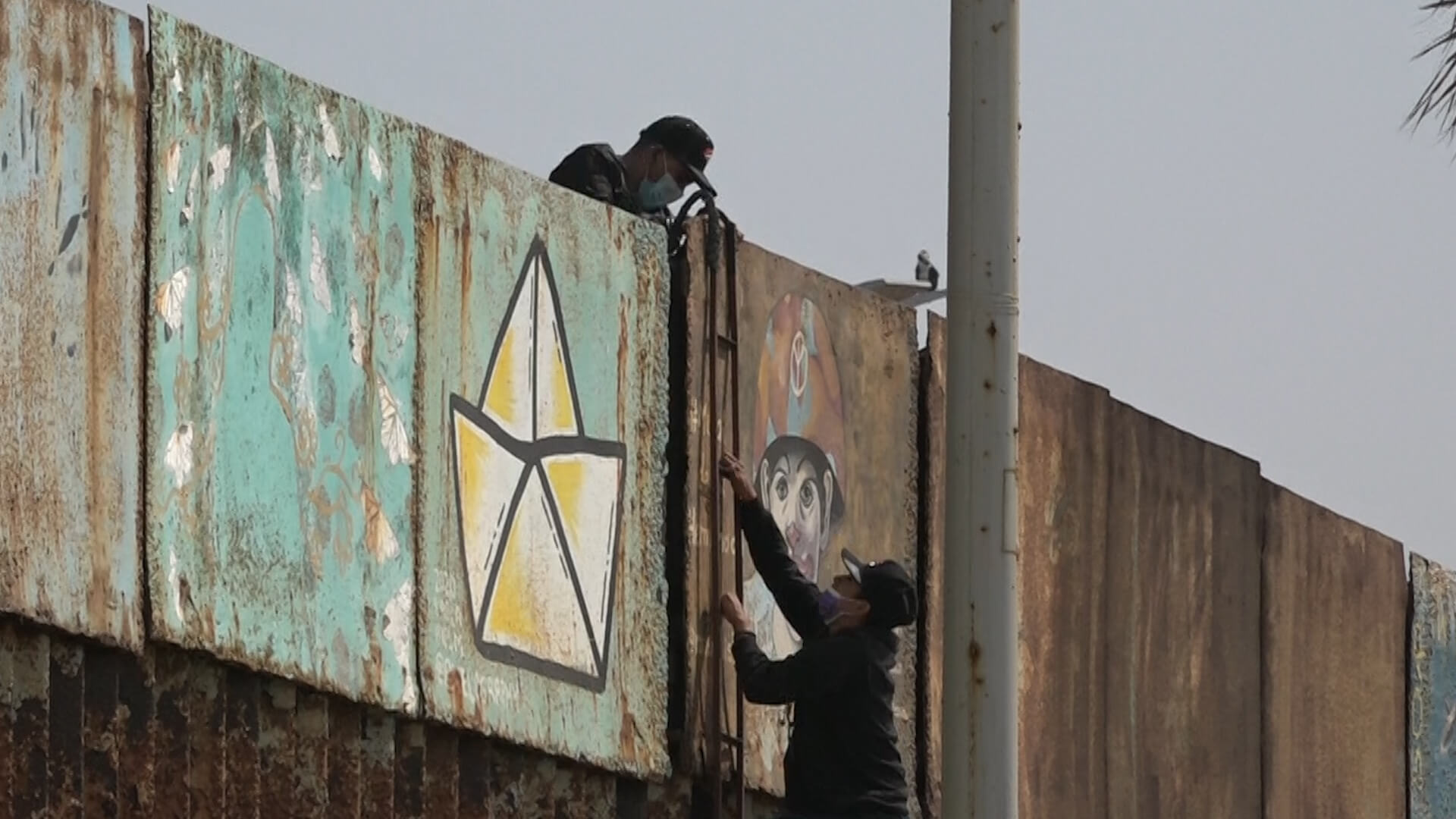 Migrantes escalando el muro de EU con una escalera desde Tijuana